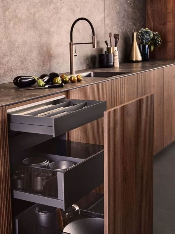 Cuisine moderne avec tiroirs de rangement ouverts gris carbone, plan de travail en pierre foncée, et robinet élégant avec accessoires de cuisine